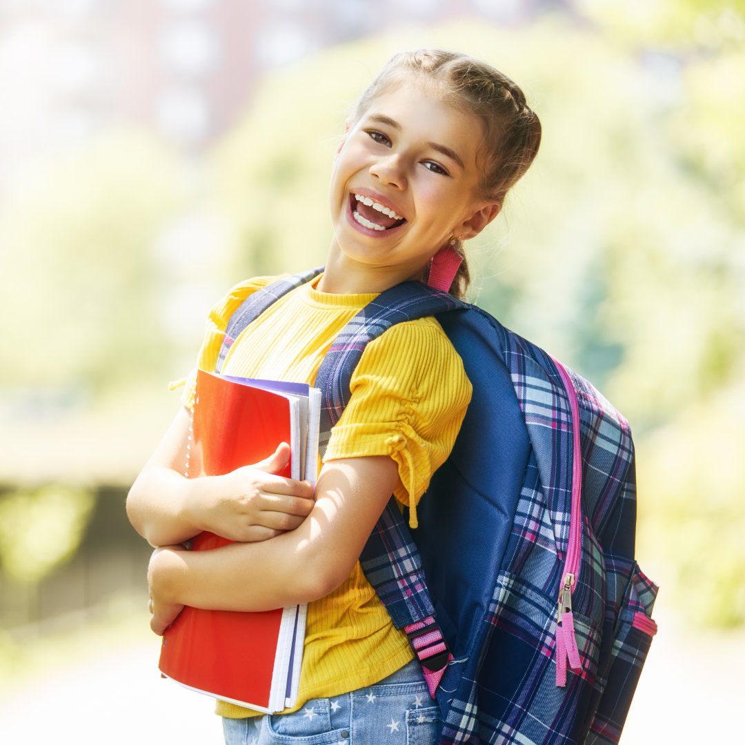 A student is walking in the summmer sun with her backpack and books.