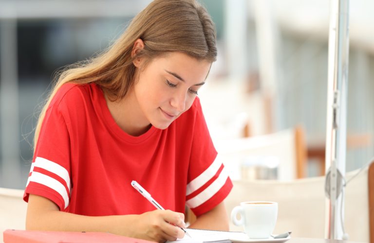 High school student writing in a notebook.